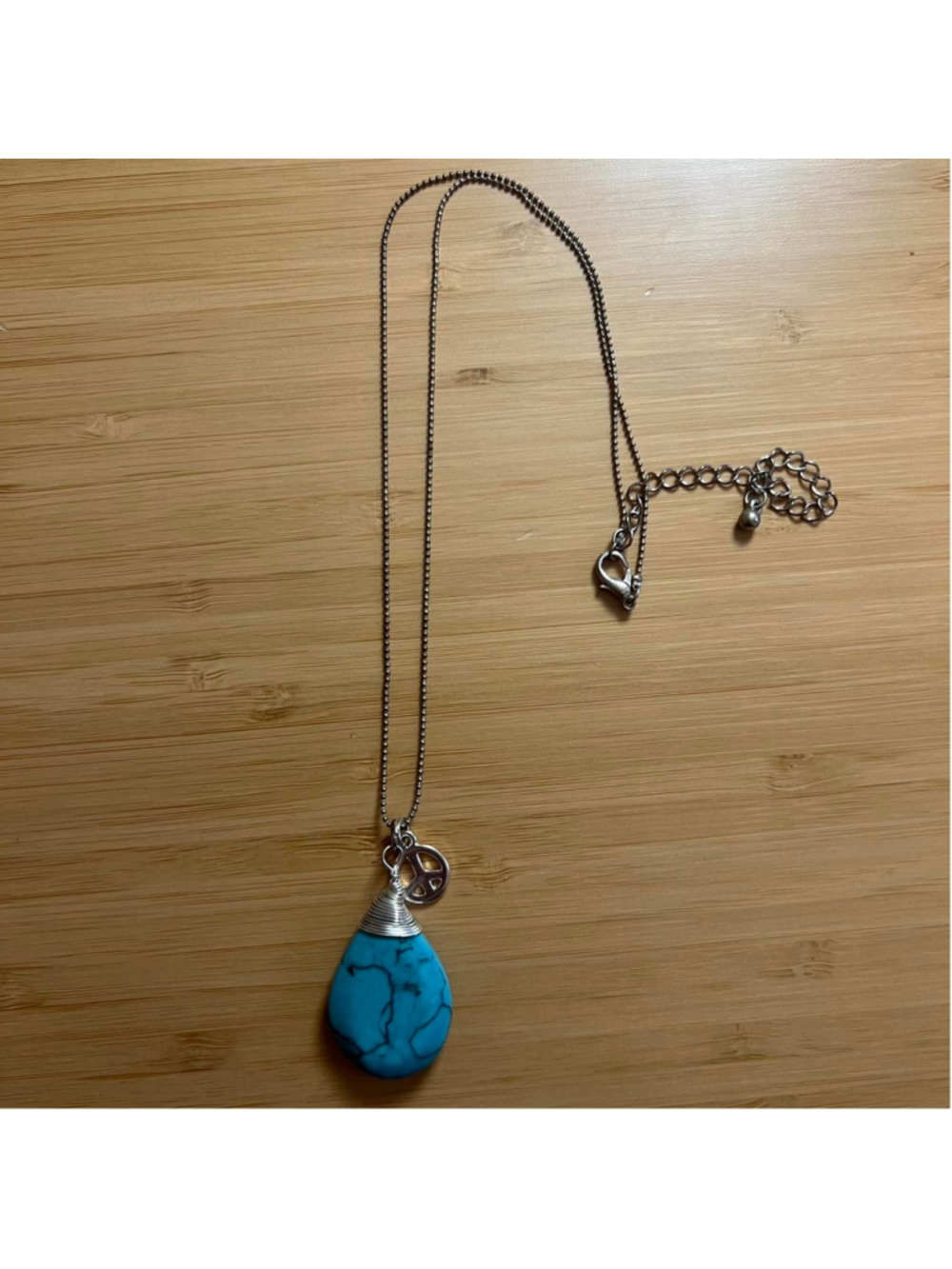 Silver necklace with turquoise-colored stone and peace sign charm